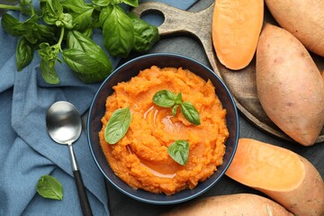 Tasty mashed sweet potato with basil in bowl, fresh vegetables and spoon on table, flat lay