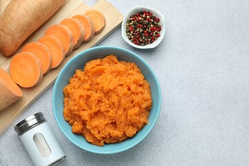 Tasty mashed sweet potato in bowl, fresh vegetables and spices on gray table, flat lay. Space for text