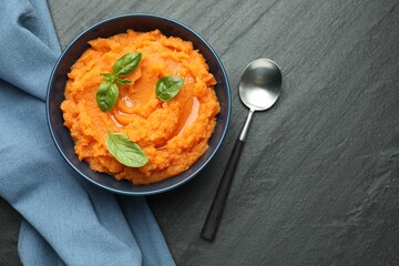 Tasty mashed sweet potato in bowl served on dark gray textured table, flat lay