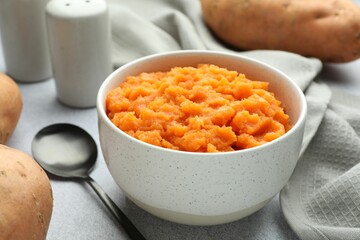 Tasty mashed sweet potato in bowl, spoon and fresh vegetables on gray table, closeup