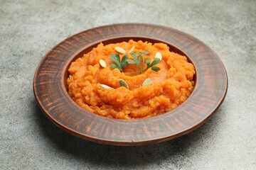 Tasty mashed sweet potato with pumpkin seeds and parsley in bowl on gray textured table, closeup