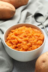 Tasty mashed sweet potato in bowl and fresh vegetables on gray table, closeup