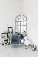 A stylish corner in a modern room featuring a vintage chair, large mirror, and decorative items in a bright, airy atmosphere