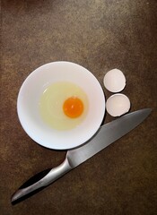 A hand cracks an egg into a bowl knife lies nearby.