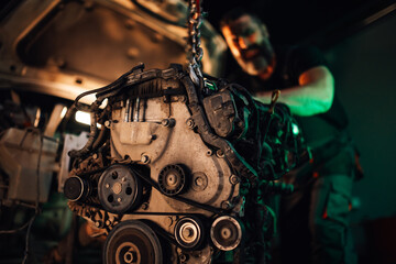 Mechanic attaching engine to car's body within a spacious workshop.