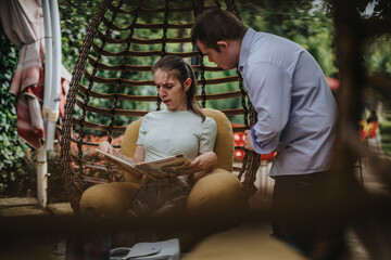 Fototapeta premium A boy with Down syndrome assists a disabled girl in reading a book while they enjoy time together in a comfortable outdoor setting.