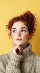 Young irish woman with red hair in a turtleneck sweater gazes up thoughtfully with freckles on her face against yellow backdrop, perfect for fashion or beauty themes; looking doubtful with copy space