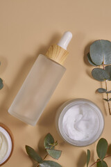 Set of beauty products in glass and bamboo bottles on beige background surrounded eucalyptus leaves. Skin care set for daily routine. Mockup for designers
