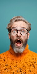 Man with a beard and glasses is making a surprised face with a wide open mouth while standing in front of a blue background; shock and astonishment expression; amazement and disbelief stare; wow 