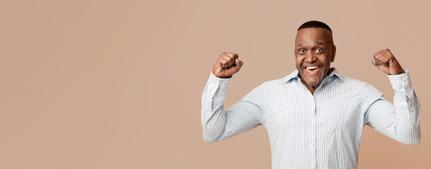 Strong middle aged african american man showing biceps at camera, orange panorama background