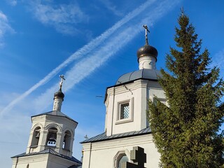 Traces of a chemtrail in the sky against the backdrop of religious sites - an Orthodox church and a mosque