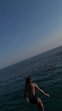 Brave young girl jumping off a cliff into the clear sea.