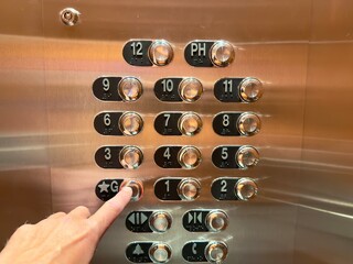 A hand presses the silver button inside an elevator