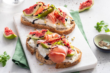 Two slices of bread with figs and ham on top of a white plate