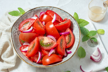 A bowl of tomatoes and onions with basil on top