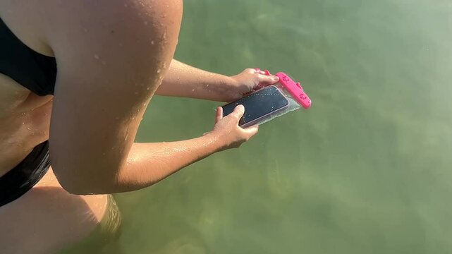 A woman with light skin using a waterproof phone case in a lake, enjoying summer holidays and technology