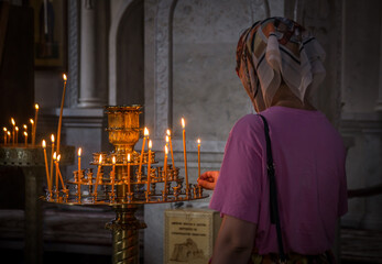 Praying woman, putting a lit candle onto a golden stand in Russian orthodox cathedral