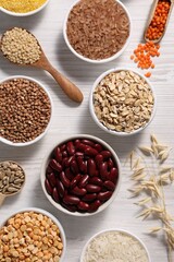 Different types of cereals, seeds and legumes on white wooden table, flat lay