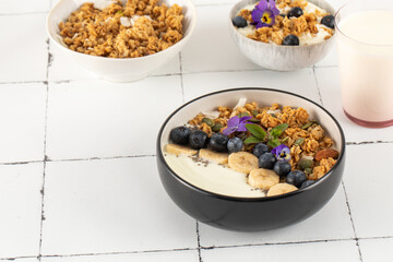 A healthy nutritious breakfast of natural Greek yoghurts, granola and fresh berries on tile background.