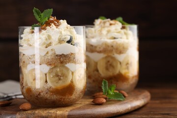 Tasty trifle dessert. Sponge cake, banana and whipped cream in glasses on wooden table, closeup