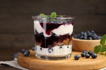 Tasty trifle dessert. Blueberries, sponge cake and whipped cream in glass on wooden table