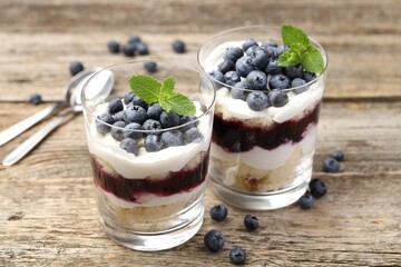 Tasty trifle dessert. Sponge cake, blueberries, jam and whipped cream in glasses on wooden table, closeup