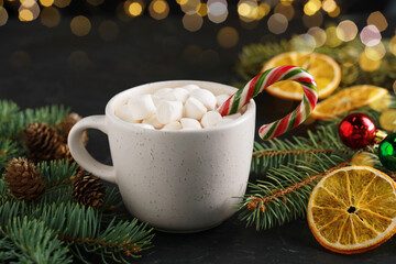 Tasty hot cocoa drink with marshmallows, candy cane in cup and Christmas decor on table, closeup