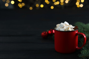 Tasty hot cocoa drink with marshmallows in mug and fir branches on black wooden table, closeup. Space for text