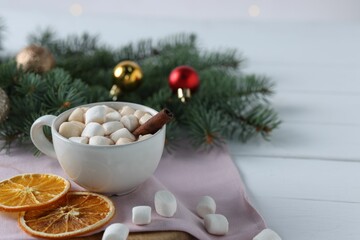 Yummy cocoa with marshmallows in cup, dried orange slices and Christmas wreath on white wooden table. Space for text
