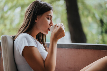 A serene scene of a young woman sipping coffee outdoors, enjoying a peaceful moment. The green...