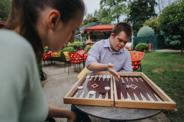 A boy with Down syndrome and a girl in a wheelchair enjoy an outdoor game of backgammon, sharing...