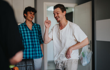 Obraz premium Two young men enjoy a lighthearted moment together, laughing and talking in a modern kitchen. The casual atmosphere highlights friendship and joy.