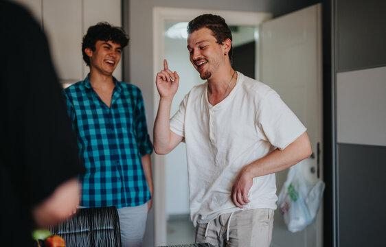 Two young men enjoy a lighthearted moment together, laughing and talking in a modern kitchen. The casual atmosphere highlights friendship and joy.