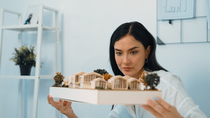 Close up of skilled young beautiful caucasian architect lift house model to check and focus on...