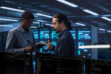 Engineers in data center using tablet and laptop to check for server performance issues arising due...