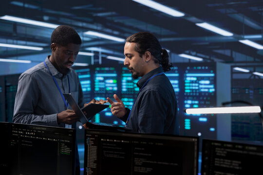 Engineers in data center using tablet and laptop to check for server performance issues arising due to high CPU usage. Server hub workers fixing insufficient memory errors slowing down hardware
