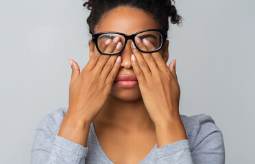 African girl in glasses rubs her eyes, suffering from tired eyes, ocular diseases concept