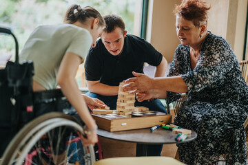 An elderly woman, a girl in a wheelchair, and a boy with Down syndrome enjoy a building blocks...