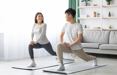 Obraz premium Happy asian young couple exercising together at home, positive korean man and woman in sportswear standing on fitness mat, stratching and having conversation, copy space. Healthy lifestyle concept