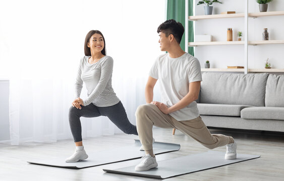 Happy asian young couple exercising together at home, positive korean man and woman in sportswear standing on fitness mat, stratching and having conversation, copy space. Healthy lifestyle concept