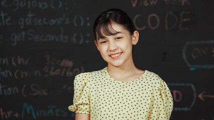 Cute happy girl smiling to camera while standing at blackboard with engineering prompt or coding,...