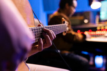 Naklejka premium Talented artist playing new accords on his electro acoustic guitar in studio, recording new tracks with music producer in control room. Male performer composing tunes on instrument. Close up.