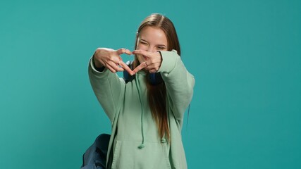 Portrait of friendly smiling woman doing heart symbol shape gesture with hands, being affectionate. Cheerful nurturing person showing love gesturing, isolated over studio background, camera A