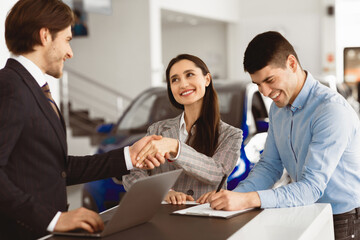 Young Spouses Buying Car, Beautiful Wife Handshaking With Seller Man Standing In Dealership Office. Selective Focus