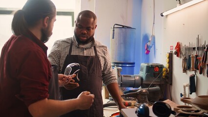 Master in woodworking shop giving BIPOC worker protection gloves before assembling furniture. Cabinetmaker preparing safety equipment for african american apprentice before starting work, camera B