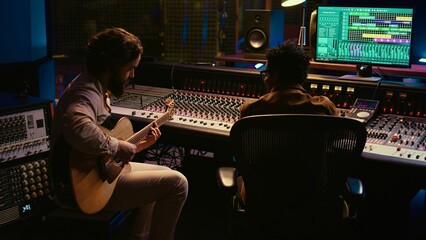 Skilled guitarist recording his electro acoustic guitar tunes on audio editing software, working...