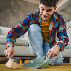 a young adult man do chores kneel and clean carpet with a broom