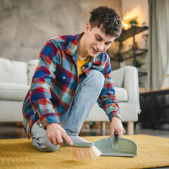 a young adult man do chores kneel and clean carpet with a broom