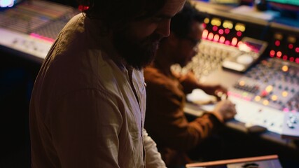 Musician playing piano midi controller in control room at professional recording studio, creating...