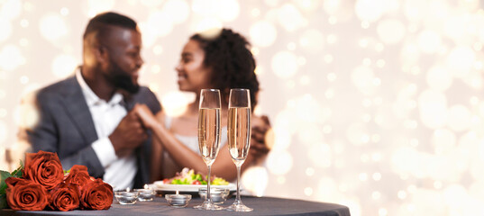 Valentine dinner. African american couple in love cuddling in restaurant, drinking champagne